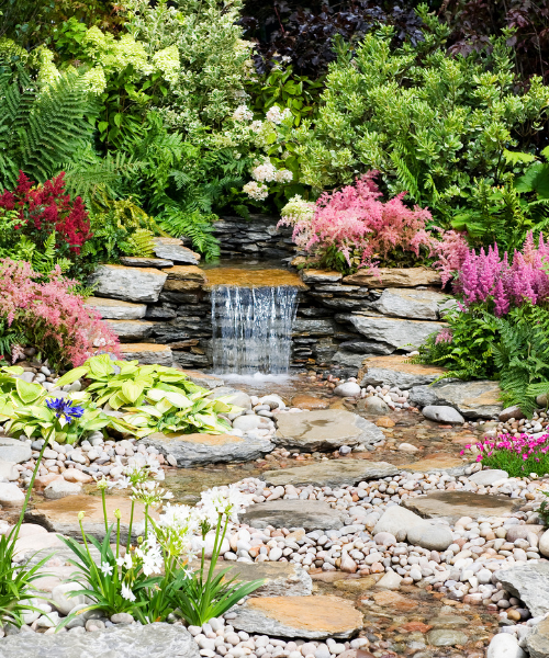 A garden with a waterfall surrounded by rocks and flowers